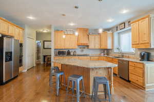 Kitchen with light wood finish cabinets, light stone counters, stainless steel appliances, pendant lighting, and a kitchen island