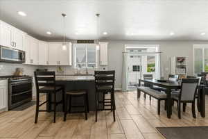 Two tone kitchen with stainless steel appliances, a breakfast bar area, a center island, pendant lighting, and light stone counters