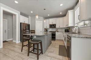 Kitchen with light stone countertops, a kitchen breakfast bar, dual tone cabinetry, stainless steel appliances, and a kitchen island