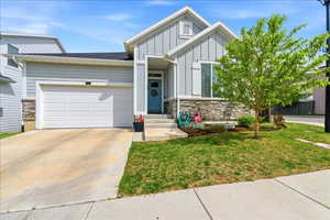 View of front facade featuring stone siding, board and batten siding, an attached garage, and concrete driveway