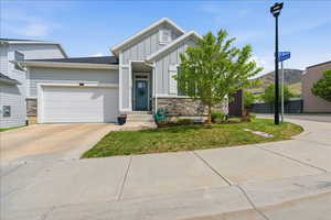 View of front of property featuring stone siding, board and batten siding, an attached garage, driveway, and a front lawn