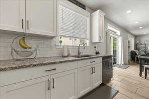 Kitchen with light stone countertops, backsplash, white cabinetry, recessed lighting, and wood tiled floors