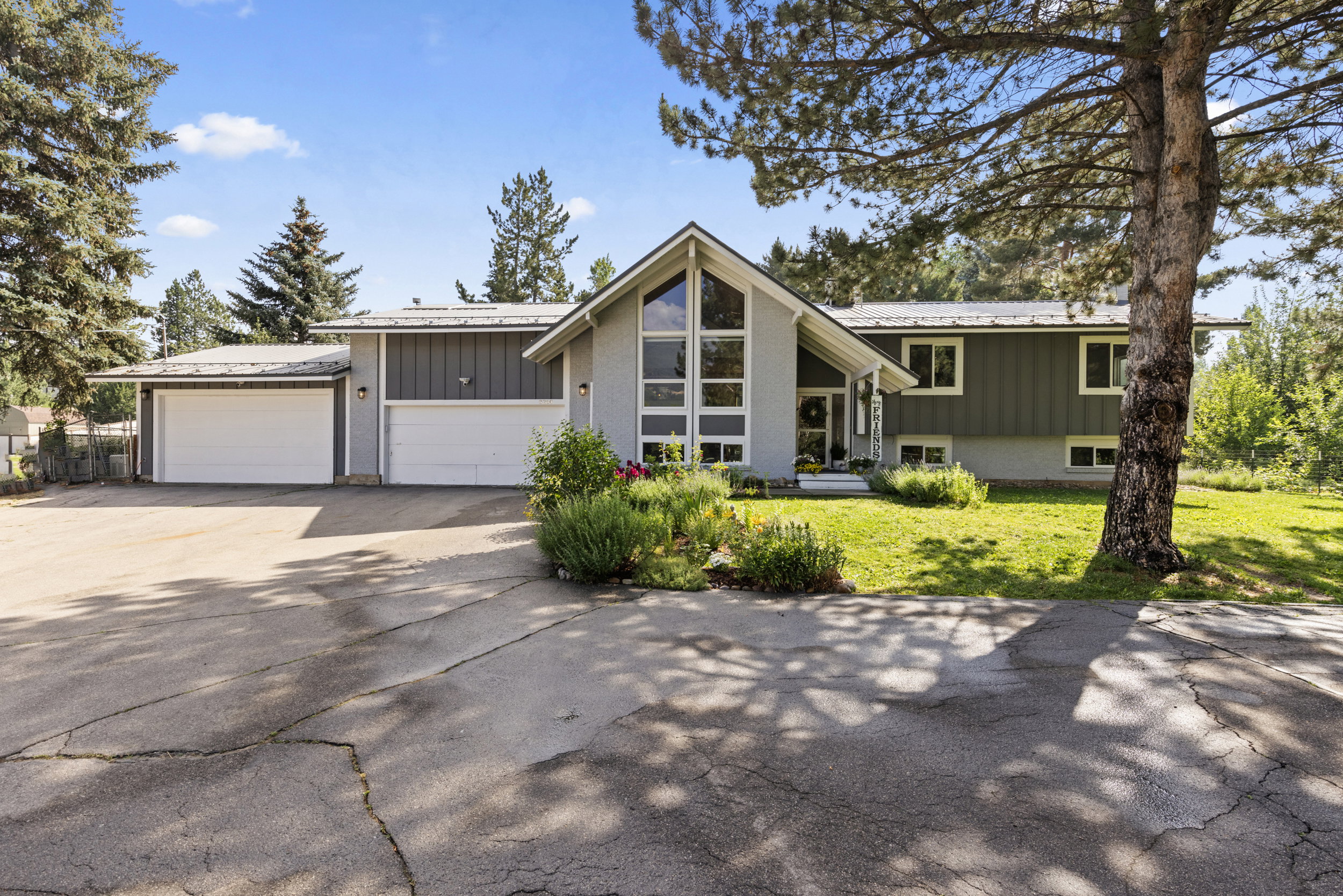 Split-level residence featuring a gray and light gray exterior, a two-car garage, and a peaked entry with tall windows