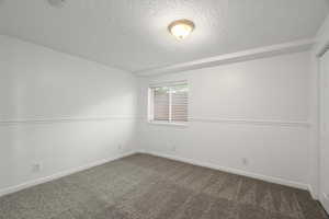 Unfurnished room with a textured ceiling and dark carpet