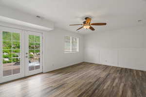 Empty room with french doors, dark wood finished floors, ceiling fan, a decorative wall, and wainscoting