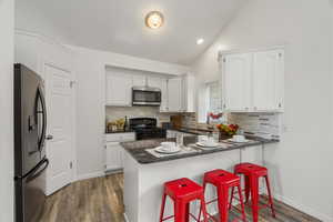 Kitchen with a kitchen breakfast bar, lofted ceiling, white cabinets, a peninsula, and stainless steel appliances