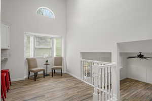 Sitting room with an upstairs landing, a ceiling fan, light wood-style floors, and a high ceiling