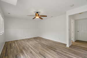 Empty room featuring dark wood-type flooring, ceiling fan, a decorative wall, and a wainscoted wall