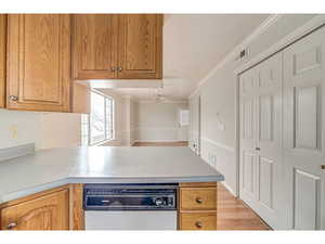 Kitchen with light countertops, ornamental molding, white dishwasher, wood finish cabinetry, and a peninsula