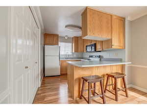 Kitchen with a kitchen breakfast bar, freestanding refrigerator, light wood-style flooring, a peninsula, and light countertops