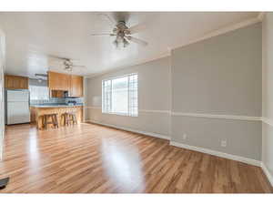 Unfurnished living room with ornamental molding, ceiling fan, and light wood-style floors