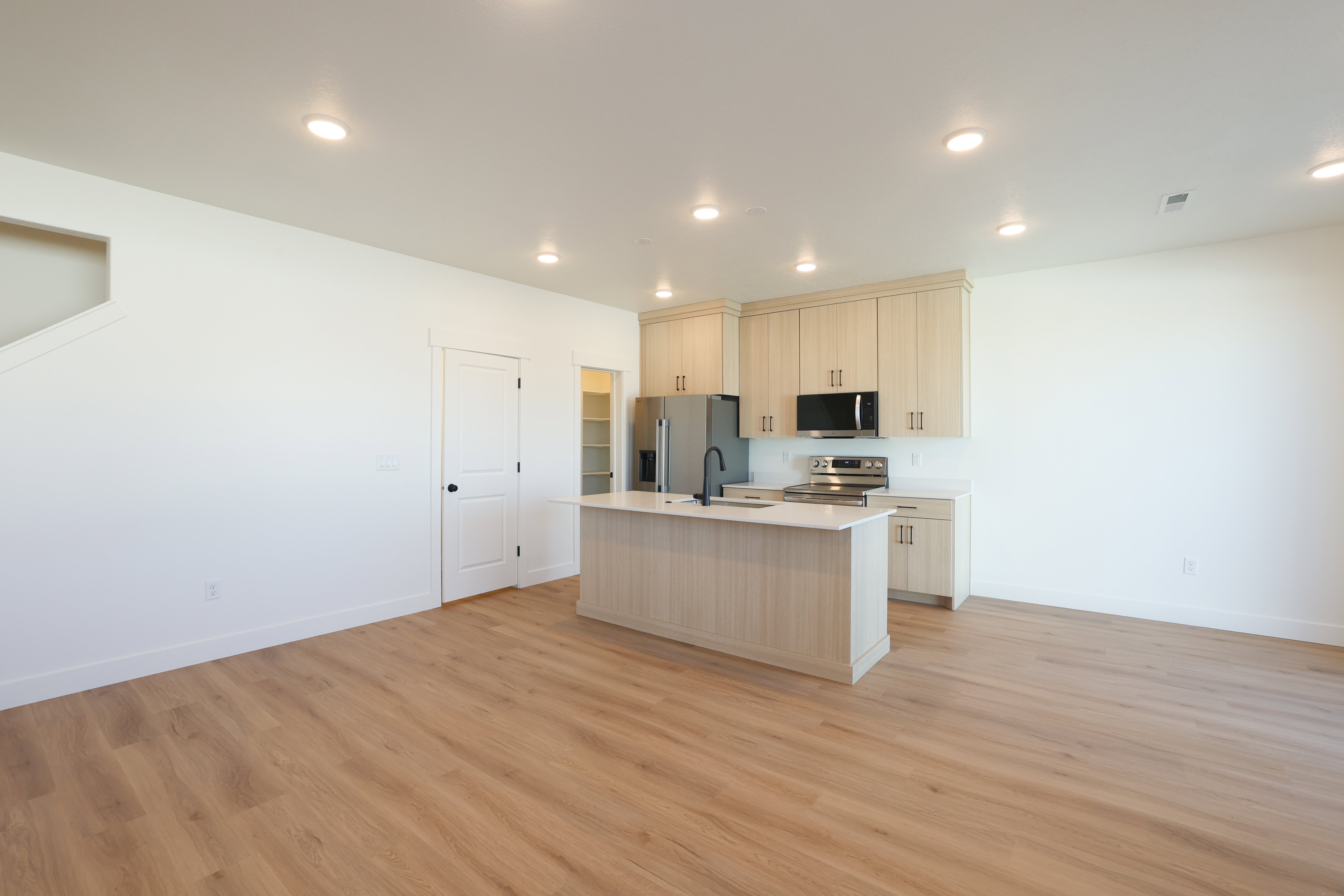 Kitchen with an island with sink, stainless steel appliances, open floor plan, light wood-type flooring, and recessed lighting