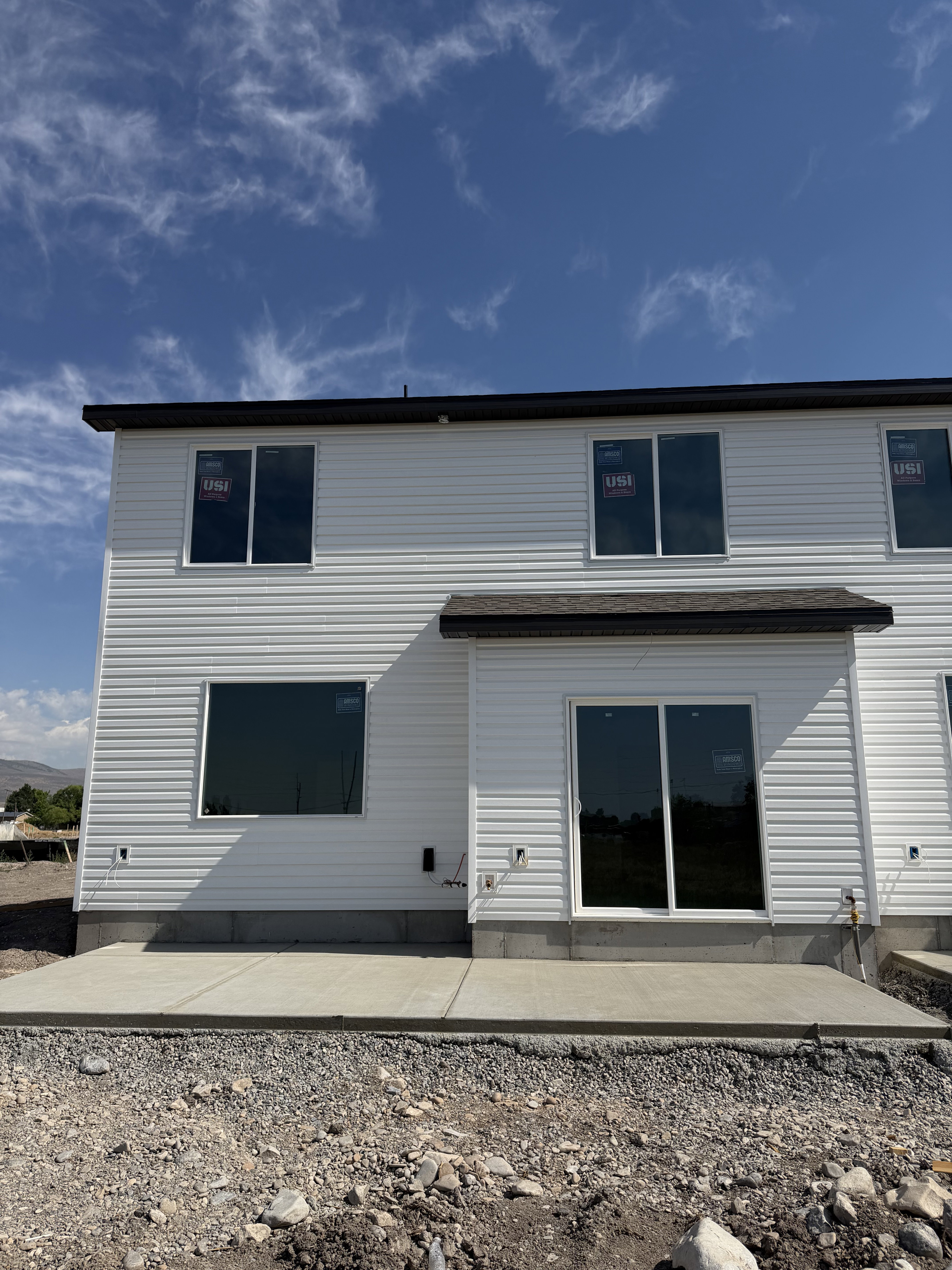 Rear exterior featuring white horizontal siding, a dark shingle roof, and a concrete patio