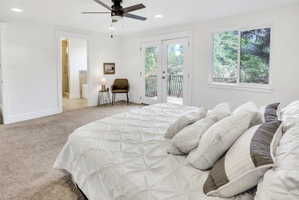 Carpeted bedroom featuring a double-pane window, ceiling fan, recessed lighting, and white French doors opening to an exterior deck