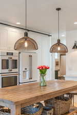 Kitchen with wood counters, white appliances, white cabinetry, and decorative light fixtures