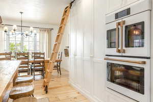 Kitchen with white double oven, light wood-type flooring, hanging lights, a barn door, and light countertops