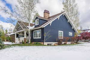 Snow covered property with a porch and a chimney