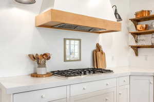Kitchen with white cabinets, stainless steel gas stovetop, open shelves, and light stone countertops