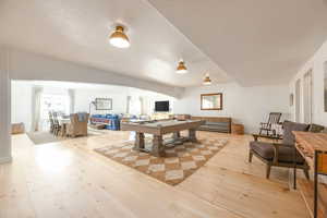 Recreation room featuring arched walkways, light wood-style floors, billiards, and a textured ceiling