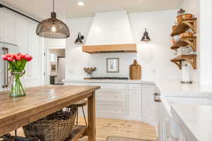 Kitchen featuring white cabinets, open shelves, light wood-type flooring, decorative light fixtures, and light stone countertops