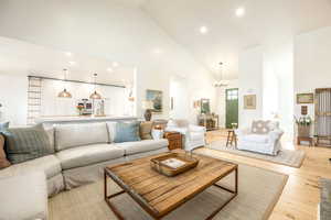 Living area featuring a chandelier, light wood-style flooring, and vaulted ceiling