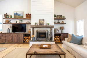 Living area featuring vaulted ceiling, light wood-style floors, plenty of natural light, and a fireplace