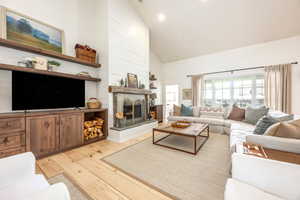 Living room featuring vaulted ceiling, light wood-type flooring, a fireplace with raised hearth, and recessed lighting
