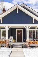 Snow covered property entrance with a chimney and a porch