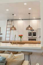 Kitchen with a breakfast bar, a textured ceiling, white cabinets, double oven, and decorative light fixtures