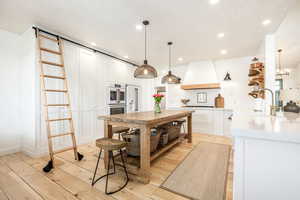 Kitchen featuring white cabinetry, light wood-type flooring, high end fridge, hanging light fixtures, and open shelves