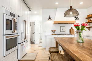Kitchen with white cabinetry, white appliances, light wood-type flooring, wooden counters, and pendant lighting