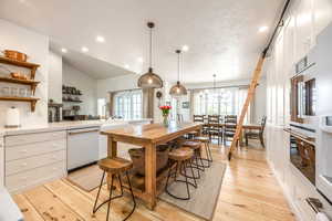Kitchen with white cabinetry, lofted ceiling, light wood-style floors, dishwasher, and a peninsula