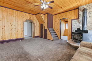 Carpeted living area featuring wooden walls, a ceiling fan, a wood stove, and wood ceiling