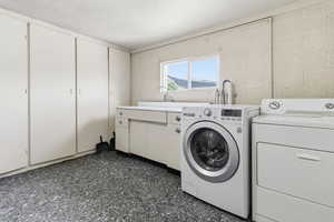 Laundry room featuring concrete block wall, washer and clothes dryer, and cabinet space