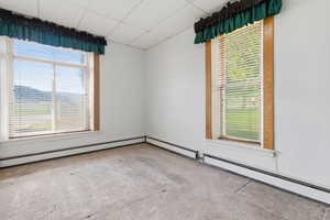 Unfurnished room featuring a baseboard radiator, a paneled ceiling, light colored carpet, and healthy amount of natural light