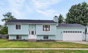 Raised ranch featuring an attached garage, concrete driveway, a chimney, entry steps, and roof with shingles