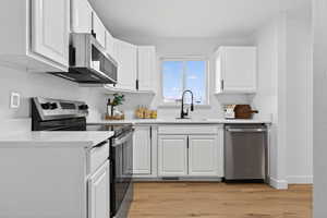 Kitchen with stainless steel appliances, white cabinetry, light wood-style floors, and light stone counters