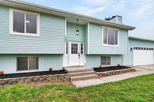 Split foyer home featuring an attached garage, a chimney, a front lawn, and driveway
