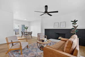 Living room featuring wood finished floors, a brick fireplace, and ceiling fan