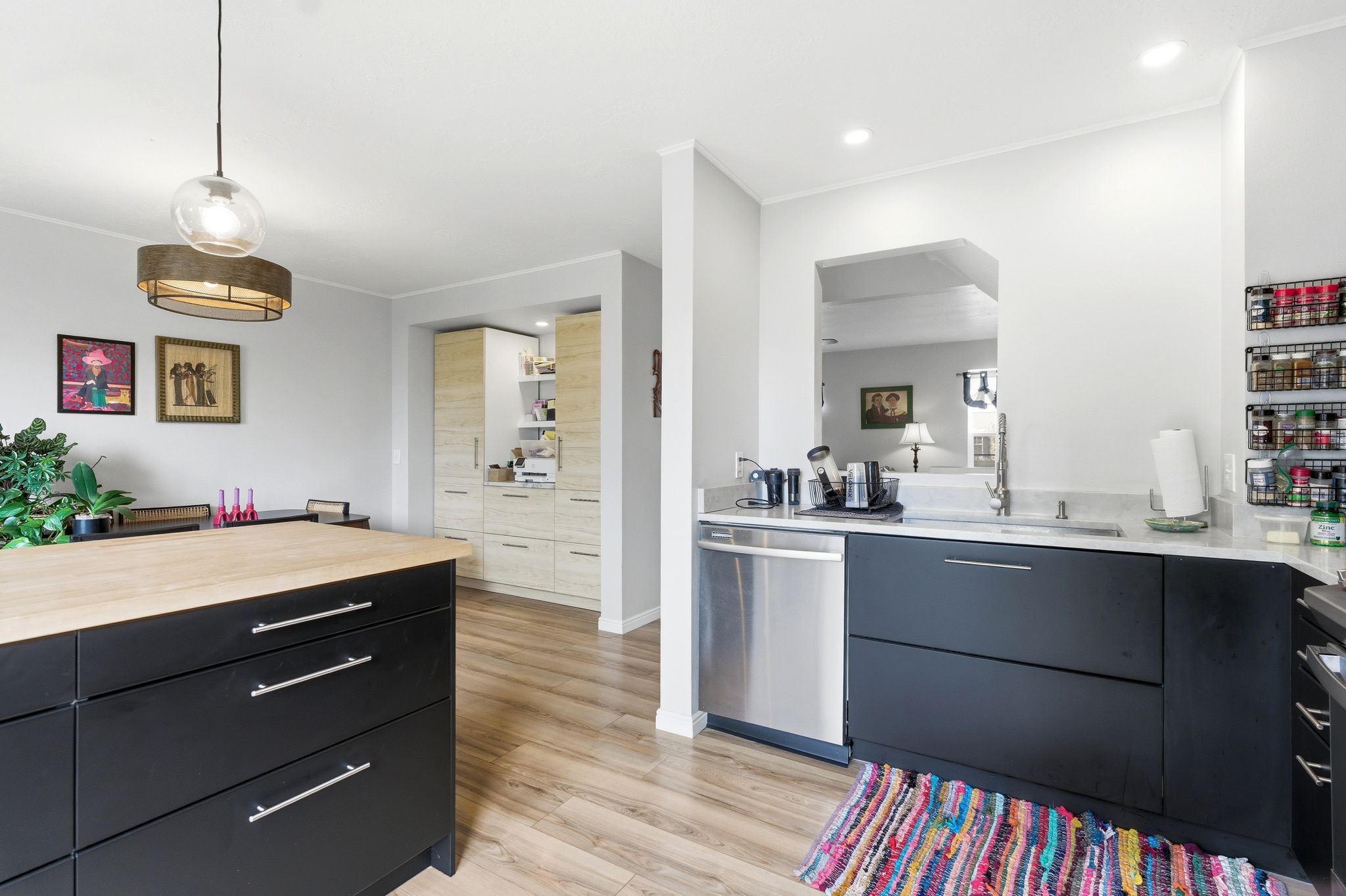 Kitchen featuring dark cabinetry, light wood finished floors, hanging light fixtures, dishwasher, and ornamental molding