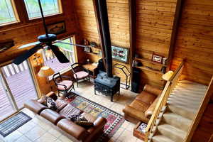 Living room with wood walls, a wood stove, a high ceiling, tile patterned floors, and a ceiling fan