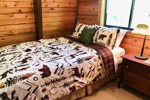Bedroom with light colored carpet and wooden walls