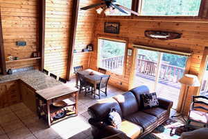 Living area with wooden walls, ceiling fan, and light tile patterned floors