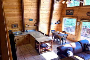 Kitchen featuring wooden walls, a peninsula, light countertops, light tile patterned flooring, and freestanding refrigerator