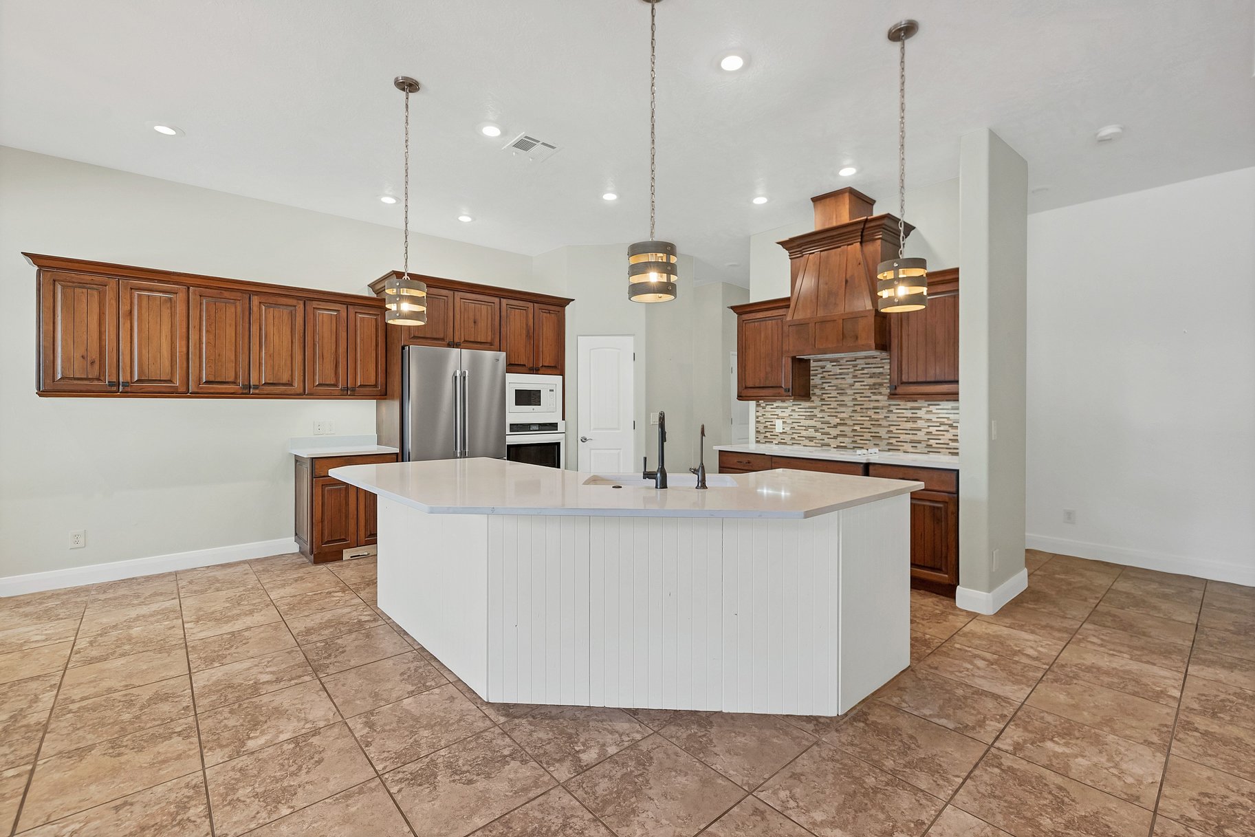 Kitchen with wood finish cabinetry, a large island, white appliances, pendant lighting, and decorative backsplash