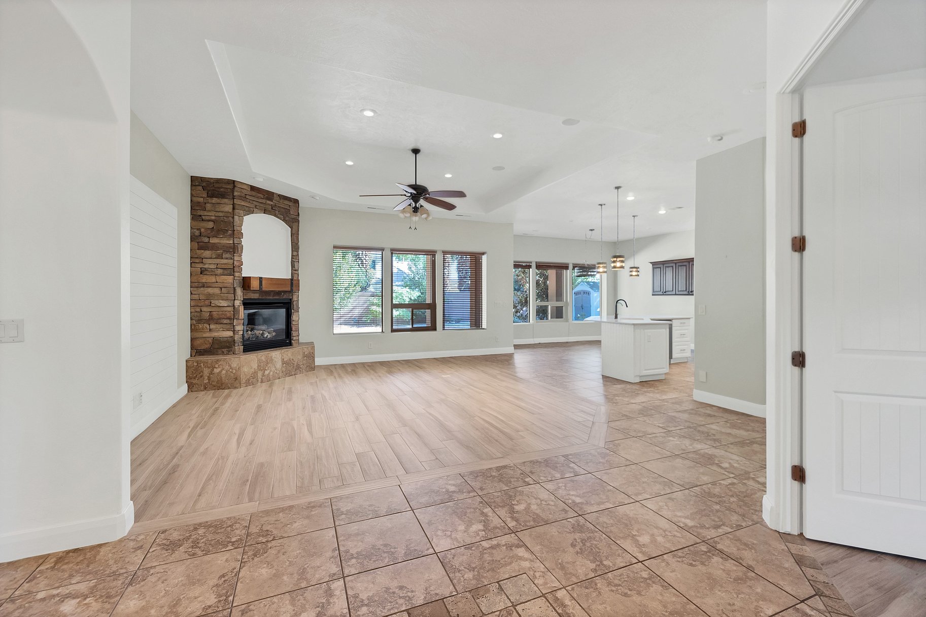 Unfurnished living room with a fireplace, a tray ceiling, a ceiling fan, light wood finished floors, and hanging lights