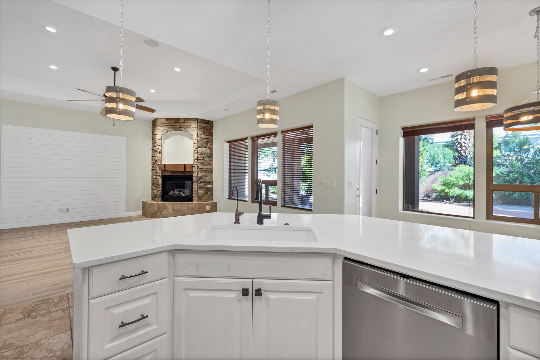 Kitchen featuring dishwasher, open floor plan, a stone fireplace, white cabinetry, and light stone countertops