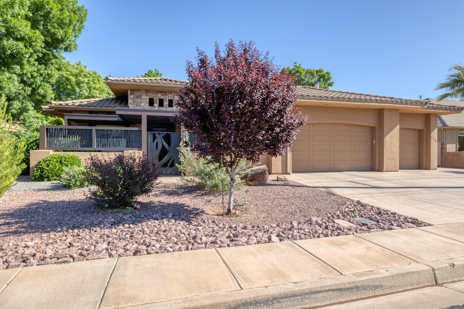 View of front of property featuring a garage, concrete driveway, a tile roof, stone siding, and stucco siding