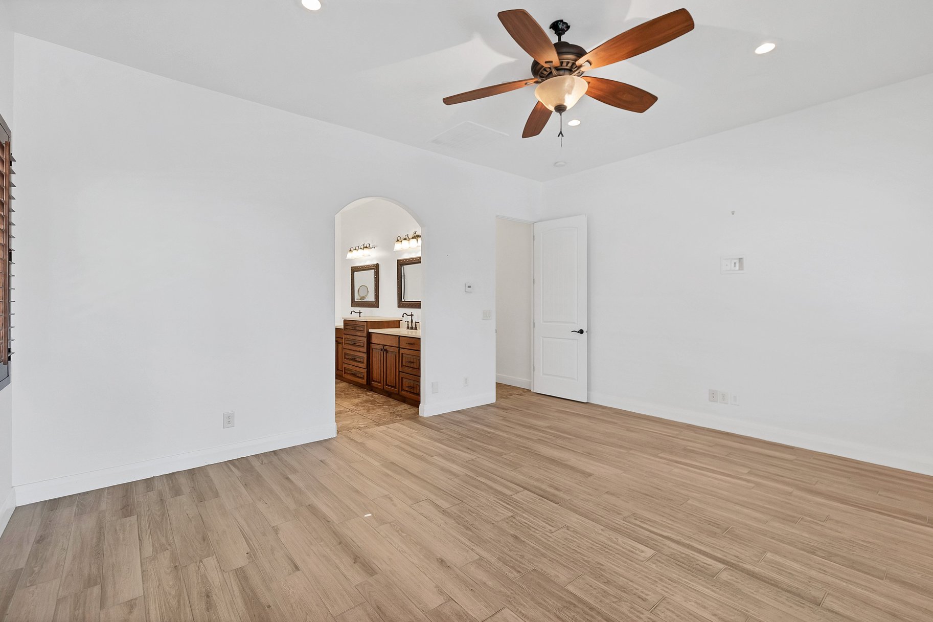 Unfurnished bedroom with light wood finished floors, arched walkways, ceiling fan, recessed lighting, and connected bathroom