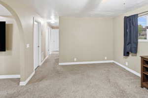 Empty room with light carpet, a textured ceiling, and arched walkways